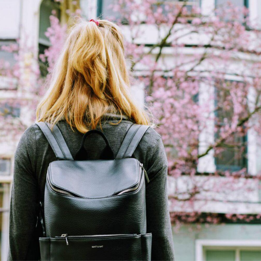 Girl standing with a backpack in front of an apartment.