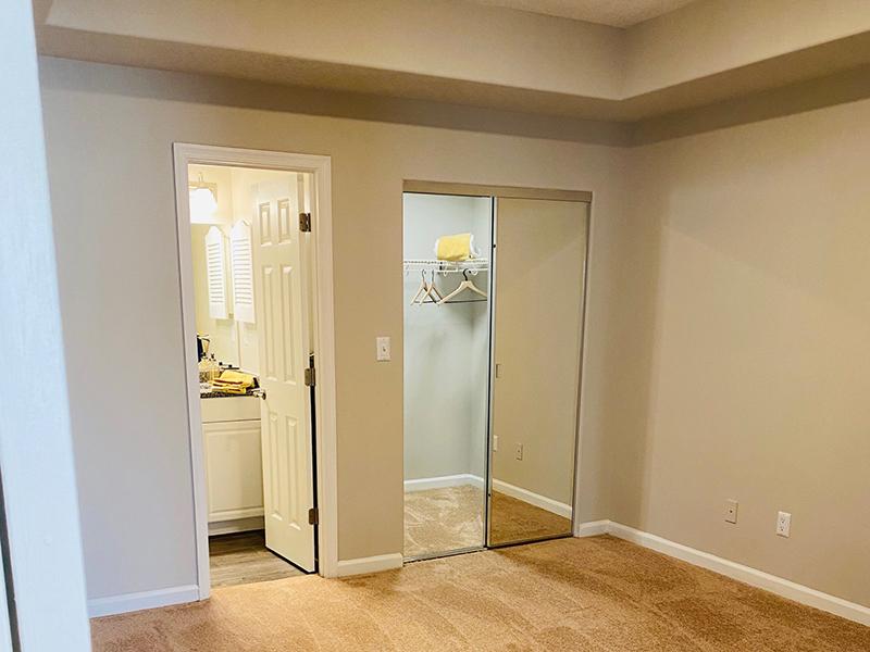 A carpeted bedroom with mirrored closet and attached bathroom at The Lakes at Town Center Apartments.