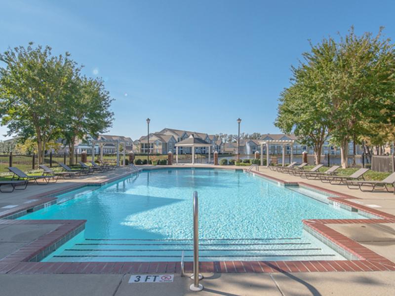A large sundeck with lounge chairs and umbrellas surround the community pool.