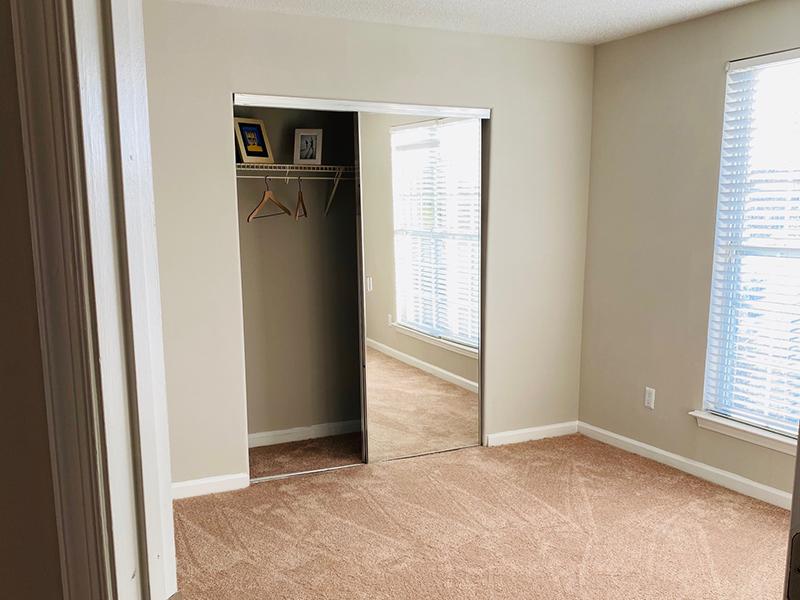 A carpeted bedroom with mirrored closet and windows covered with blinds at The Lakes at Town Center Apartments.