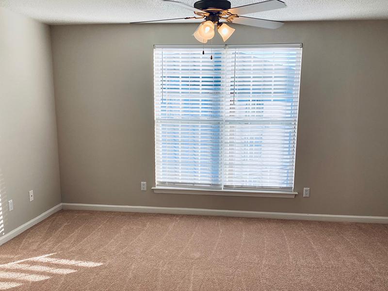 A carpeted room with a ceiling fan and window at The Lakes at Town Center Apartments. 