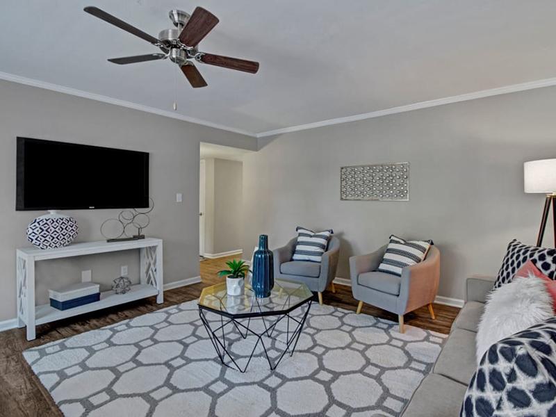 Model living room is furnished with a couch, and two chairs with a rug covering the wood-style floors.